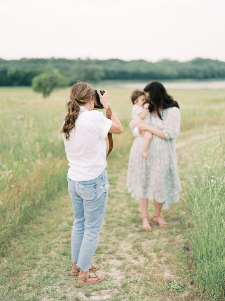 Photographer Little Rock Bailey Feeler photographing a young mother and daughter in green, grassy field.