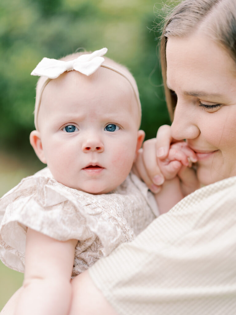 Mother holding 6 month old daughter while holding and kissing her hand taken by photographer Little Rock Bailey Feeler