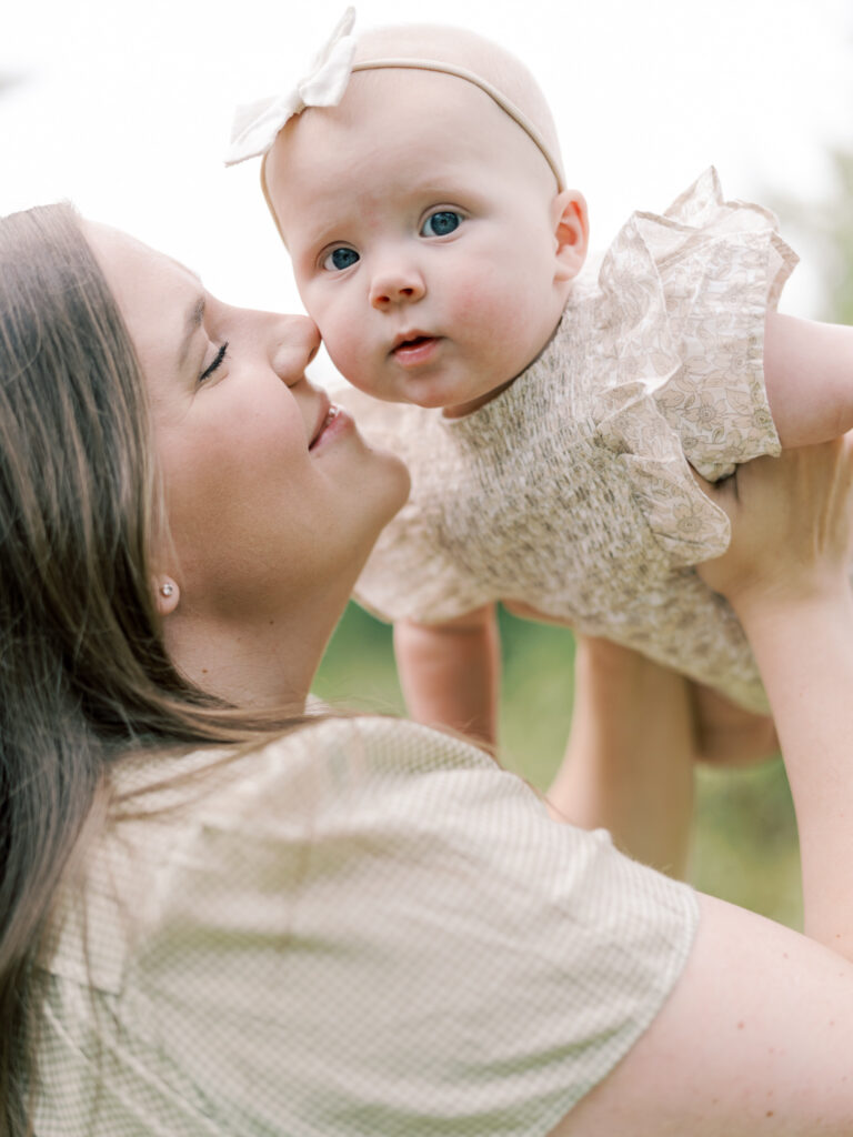 Young mother holding up her 6 month old daughter to nuzzle her cheek as a highlight to her Little Rock Motherhood Session.