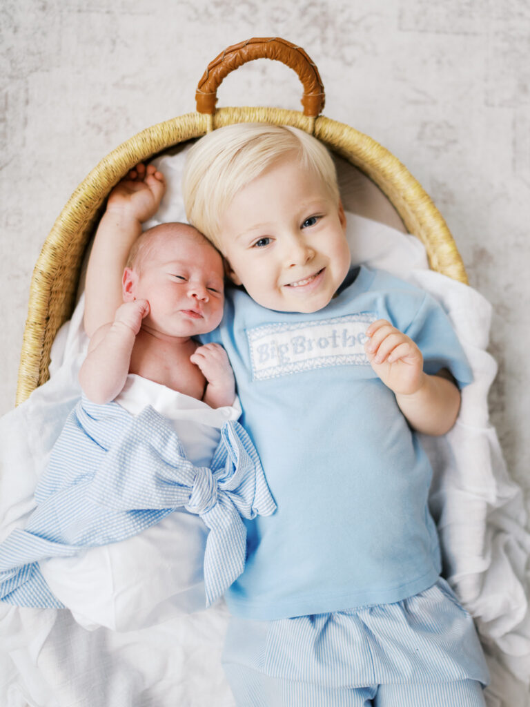 Newborn baby boy wrapped in blue bow beside big brother in studio portrait by Little Rock newborn photographer