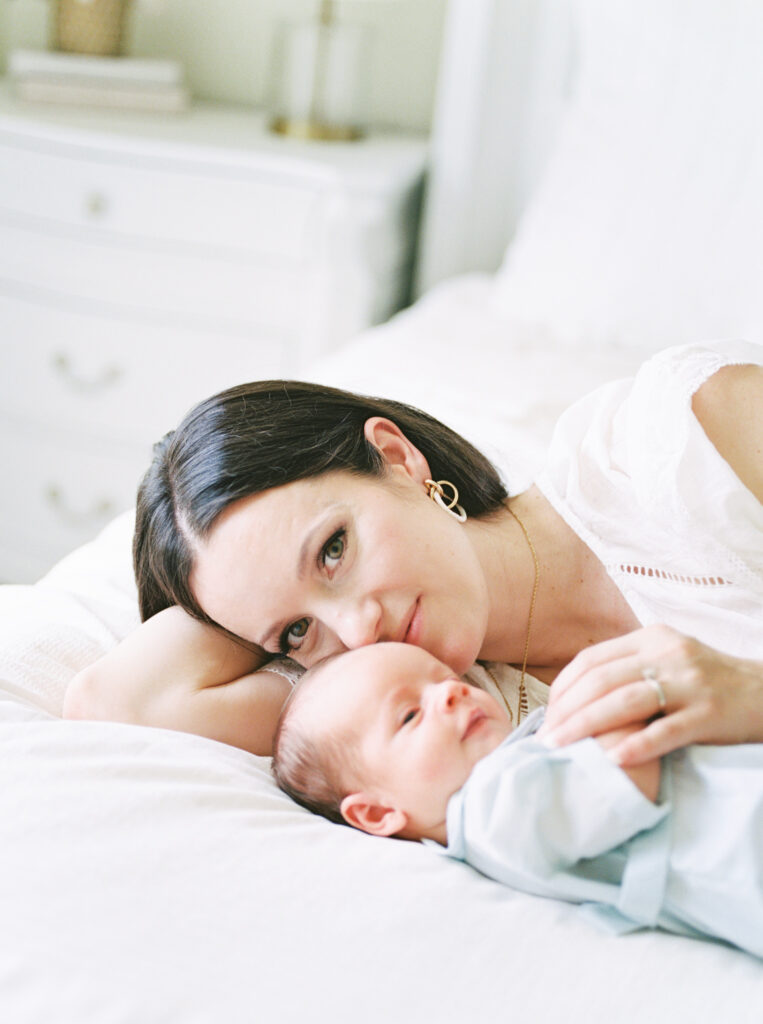 Mother snuggling newborn baby on a white bed during an in-home film family photography session in Arkansas.