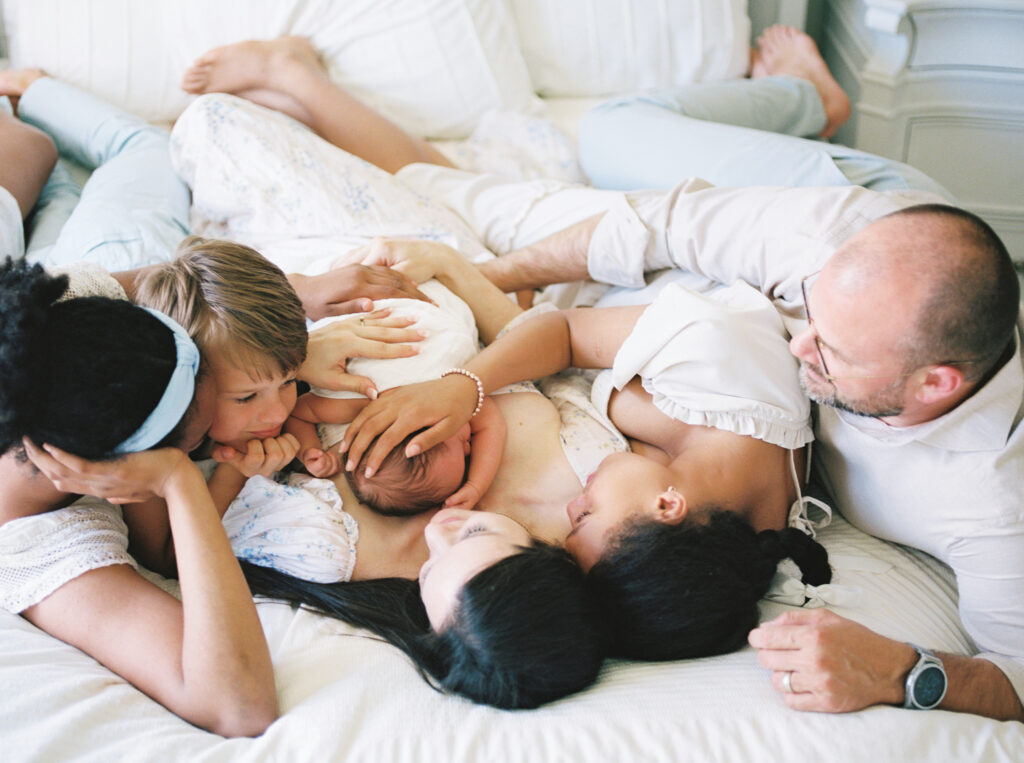Parents and children cuddling with newborn on a bed, captured on film by Bailey Feeler, family photographer in Arkansas.