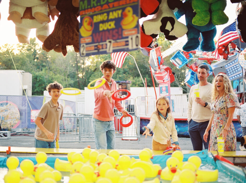 Family with teens and tweens plays toss game at the state fair - capturing genuine connection without stiff poses taken by photographer Little Rock Bailey Feeler